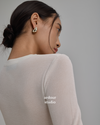 A woman shown from the back and side wearing a small gold abstract-shaped hoop earring, photographed against a plain light gray studio background - ardour studio